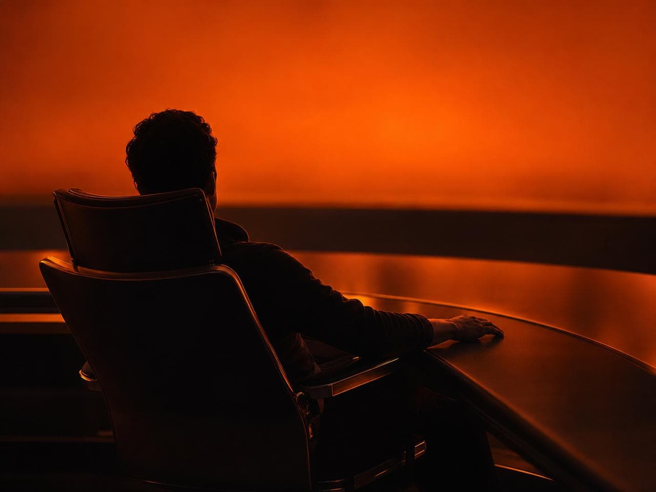 An owner sitting back at a control desk at dawn, one hand resting, while the overnight work runs without them.